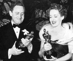 Spencer Tracy holds his Best Actor Oscar with Bette Davis beside him.